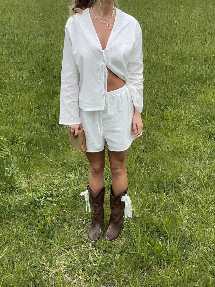 Donna in abito bianco estivo con stivali da cowboy marroni su prato verde. Moda casual, look estivo, abbigliamento femminile trendy.