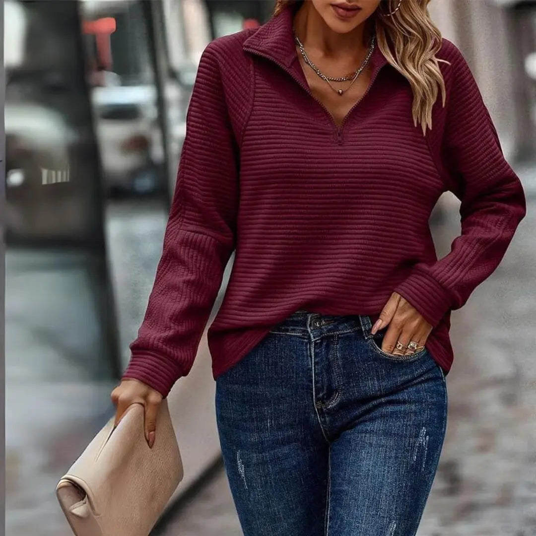 Donna con maglione bordeaux a coste, jeans blu e borsa beige. Moda autunnale casual, abbigliamento femminile elegante, strada cittadina.