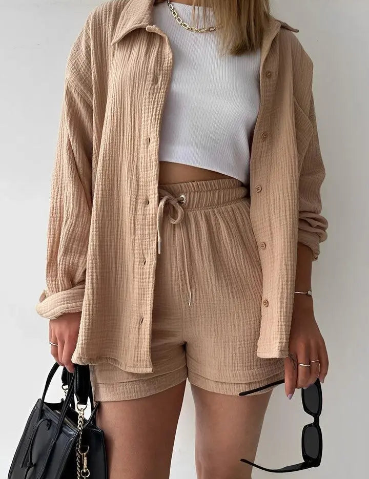 Donna con camicia beige e pantaloncini coordinati, top bianco, borsa nera e occhiali da sole. Moda casual estiva, abbigliamento femminile trendy.