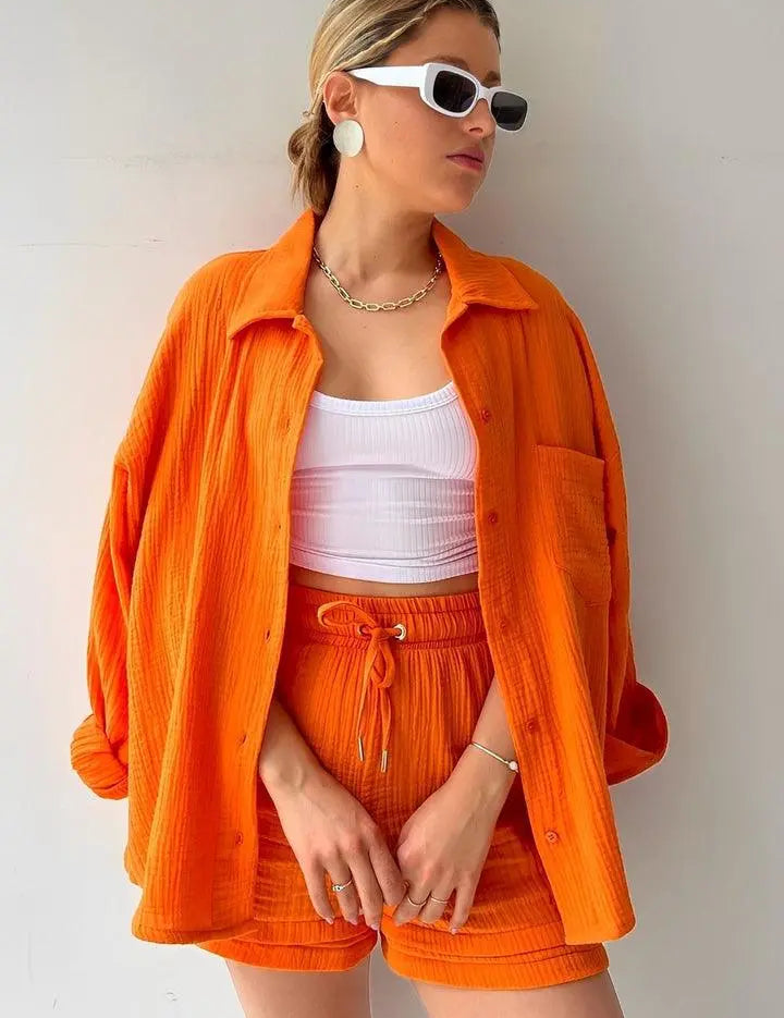 Donna con camicia e shorts arancioni, top bianco, occhiali da sole bianchi, orecchini grandi e collana. Moda estiva casual e trendy.