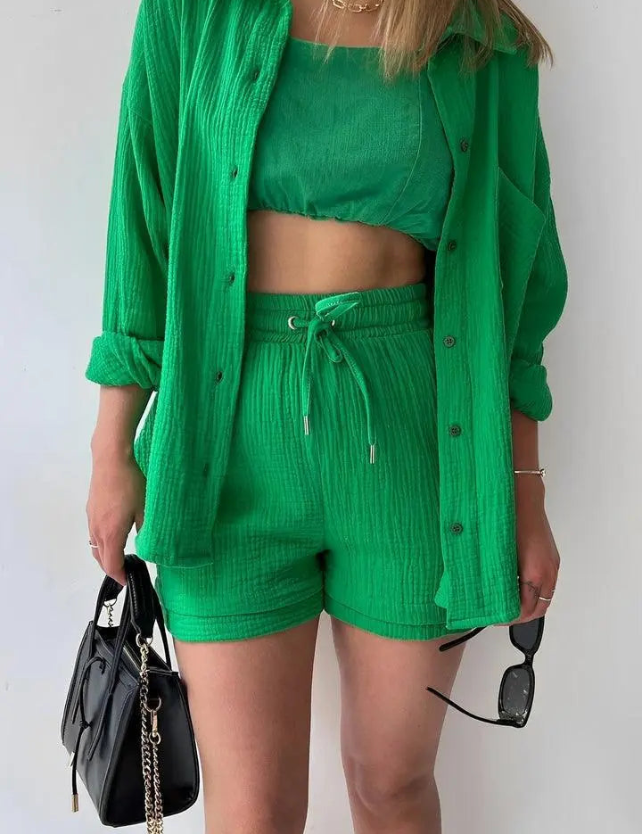 Donna con completo verde a tre pezzi: camicia, top e shorts. Accessori: borsa nera e occhiali da sole. Moda estiva, abbigliamento casual chic.