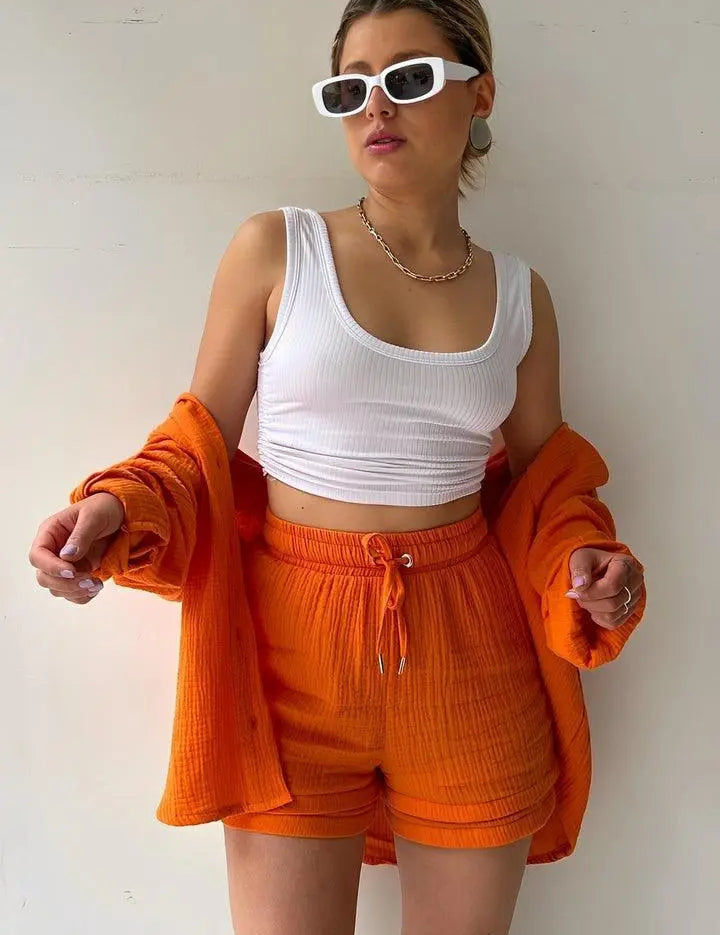 Donna con occhiali da sole bianchi, top bianco, shorts arancioni e camicia coordinata. Moda estiva, abbigliamento casual, stile trendy.
