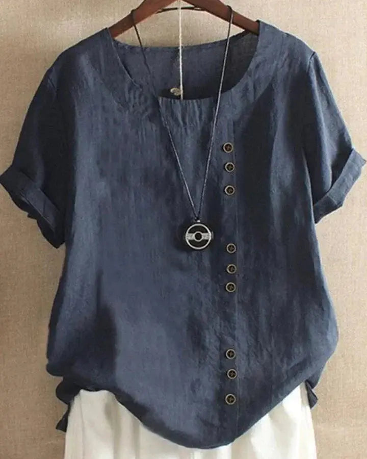 Camicia donna blu in lino con bottoni decorativi asimmetrici, maniche corte risvolte, scollo tondo, abbinata a collana pendente.