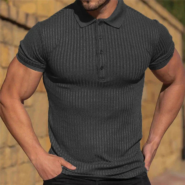 Maglietta polo uomo a righe nere, aderente, maniche corte, colletto classico, sfondo muro giallo. Moda maschile casual elegante.