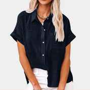 Blusa nera da donna con maniche corte, colletto classico e bottoni, abbinata a pantaloni bianchi. Stile casual elegante, moda femminile.