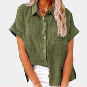 Camicia verde oliva da donna in lino, maniche corte, colletto classico, tasca frontale, abbinata a pantaloni bianchi. Moda estiva casual.