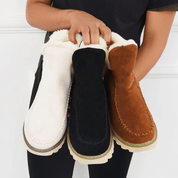 Donna che tiene stivali invernali in pelle scamosciata, colori bianco, nero e marrone, con fodera in pelliccia. Scarpe calde e alla moda per l'inverno.