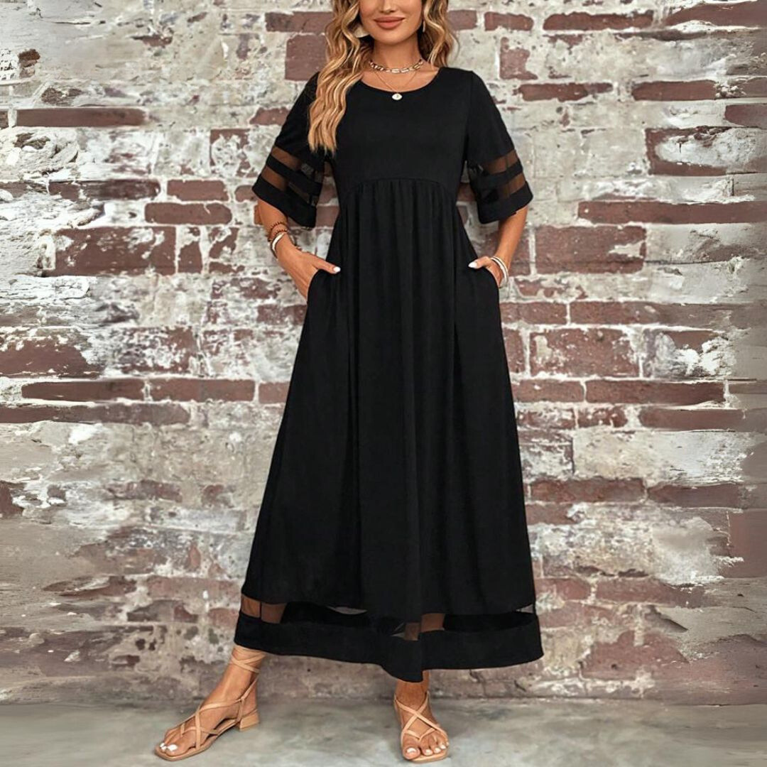 Donna con abito lungo nero elegante, maniche trasparenti, davanti a muro di mattoni. Moda femminile, abbigliamento estivo, stile casual chic.