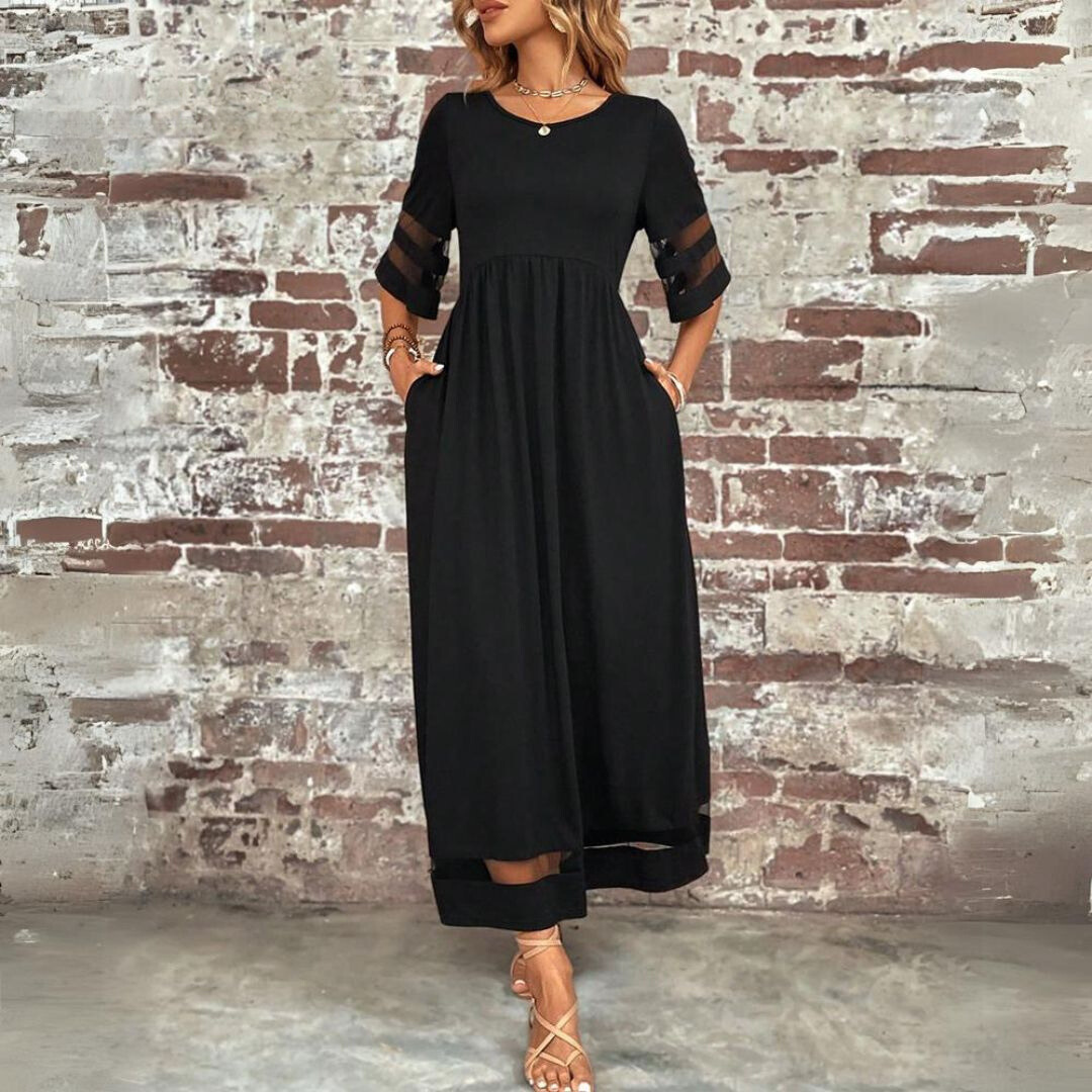 Abito lungo nero elegante da donna con maniche trasparenti, indossato con sandali beige, sfondo muro di mattoni. Moda femminile, abbigliamento estivo.