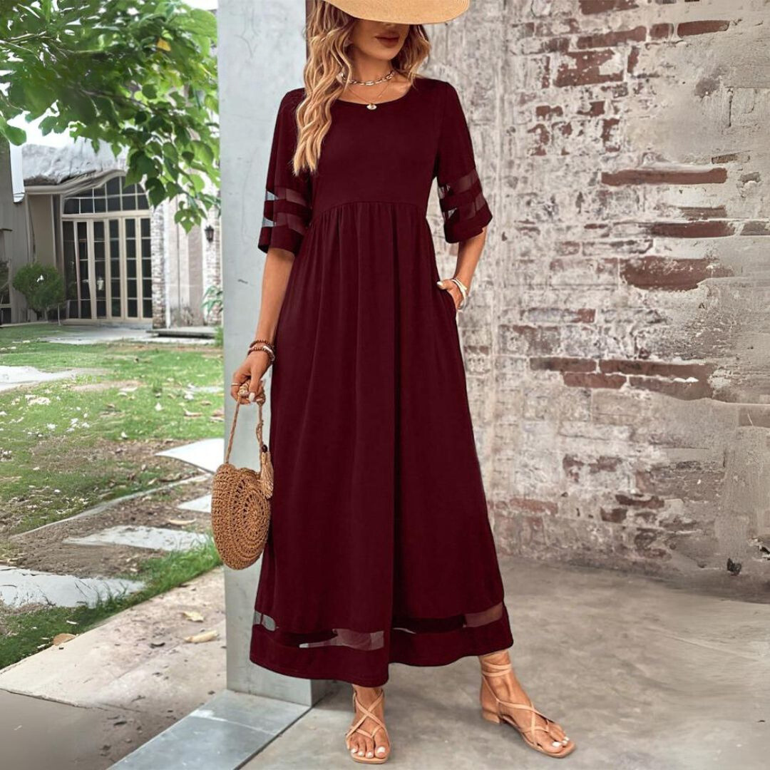 Donna con abito lungo bordeaux, maniche trasparenti, cappello di paglia e borsa rotonda in paglia. Moda estiva elegante, look casual chic.