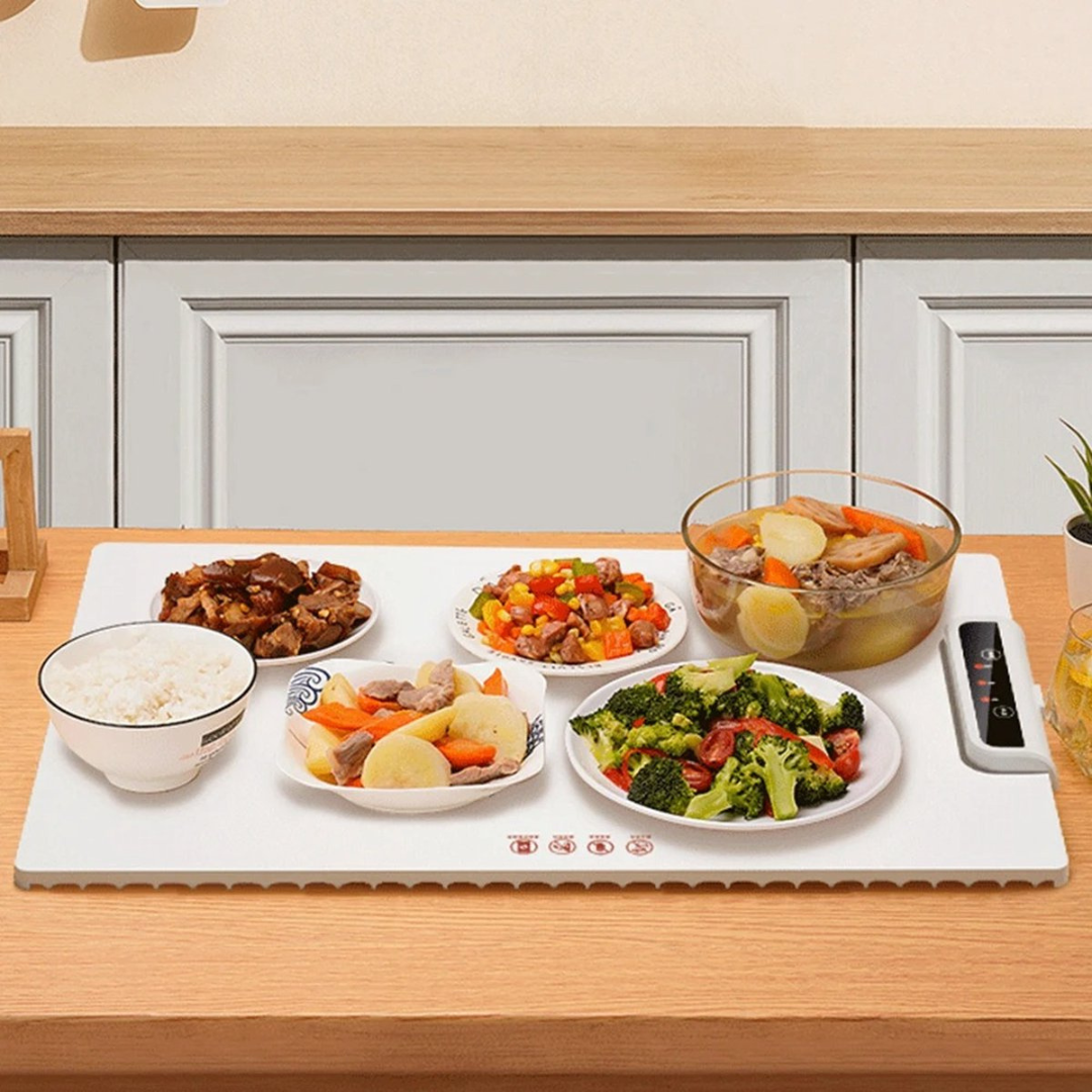 Piatto riscaldante elettrico su tavolo da cucina con ciotole di riso, stufato di carne, verdure miste e insalata, ideale per mantenere il cibo caldo.