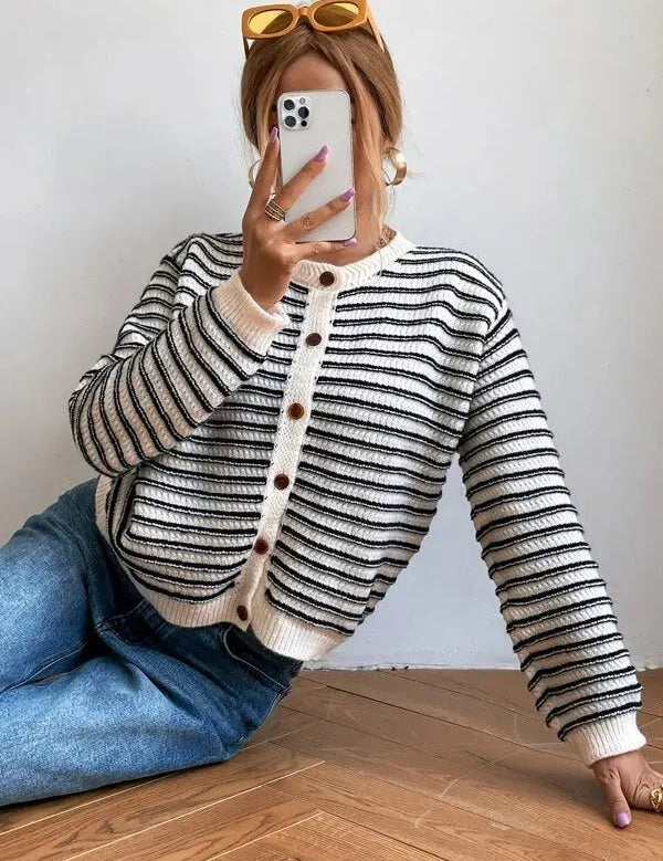 Donna con cardigan a righe bianche e nere, jeans blu, occhiali da sole gialli, scatta selfie con smartphone. Moda casual autunnale.
