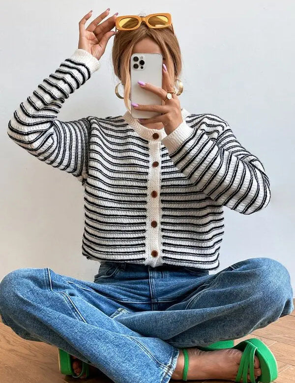 Donna con cardigan a righe bianche e nere, jeans blu e occhiali da sole gialli. Moda casual, stile autunnale, abbigliamento femminile trendy.