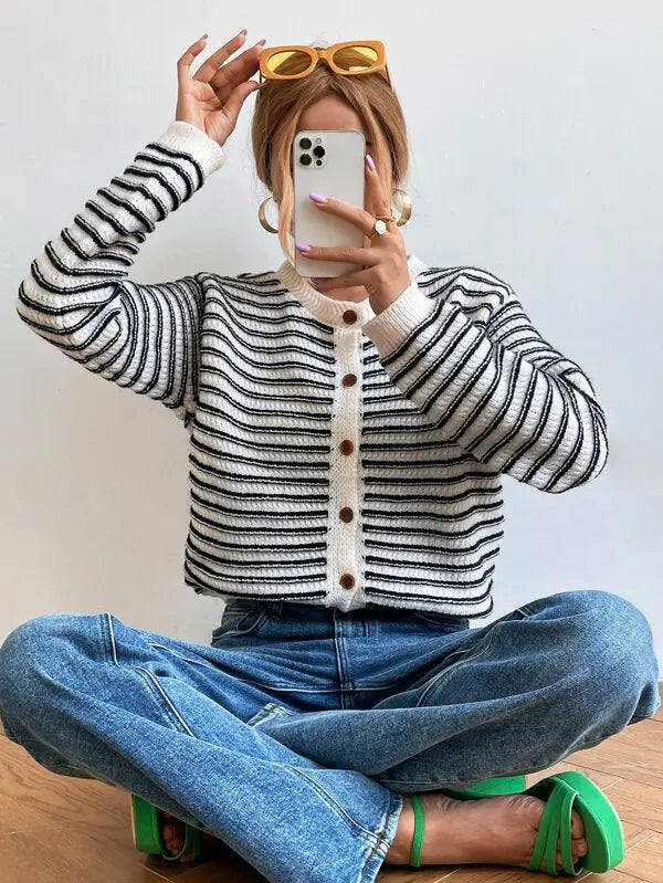 Donna con cardigan a righe bianche e nere, jeans blu e occhiali da sole gialli. Moda casual, stile autunnale, abbigliamento femminile trendy.