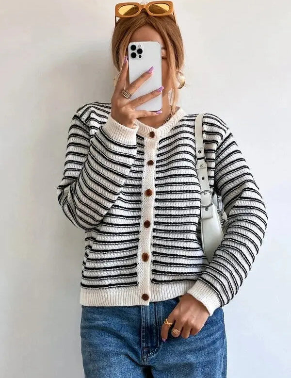 Donna con cardigan a righe bianche e nere, jeans blu, borsa bianca e occhiali da sole marroni. Scatta un selfie con smartphone bianco.