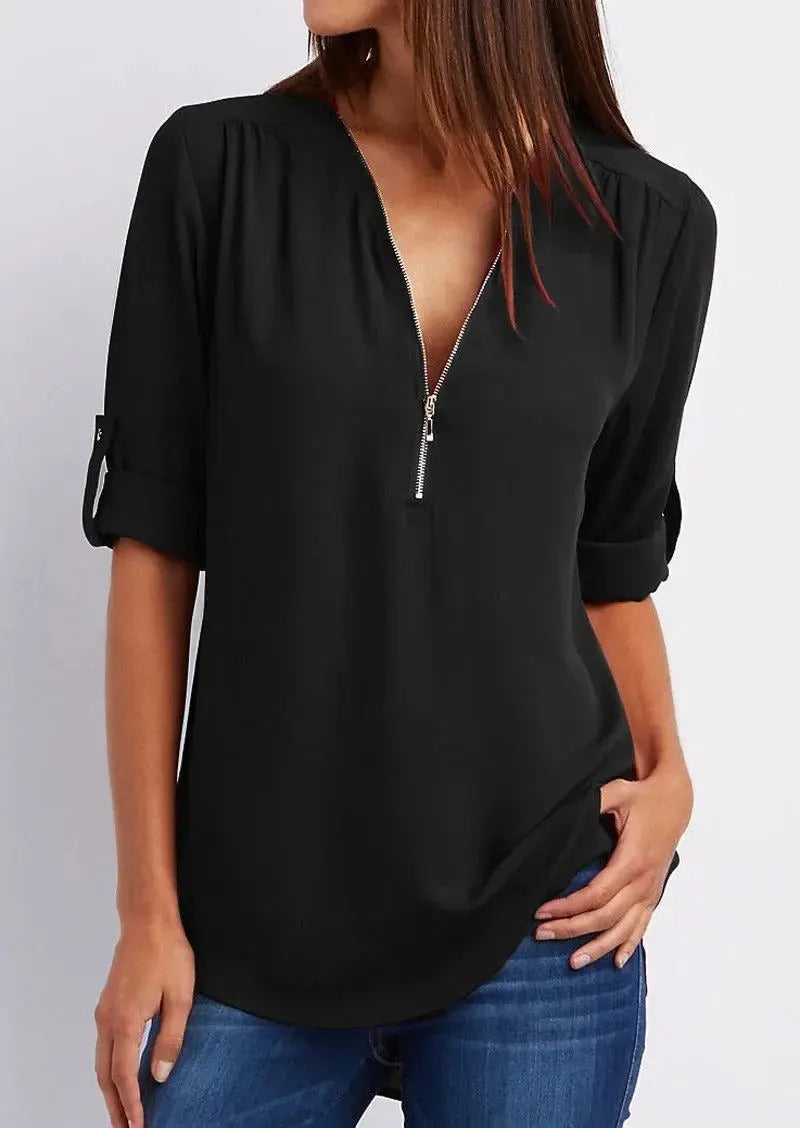 Blusa nera da donna con zip frontale, maniche a 3/4 arrotolate, scollo a V, abbinata a jeans blu. Elegante e casual, perfetta per ogni occasione.