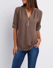 Blusa marrone con zip frontale, maniche a 3/4 arrotolate, indossata con jeans. Moda casual donna, abbigliamento autunnale elegante.