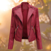 Giacca in pelle rossa da donna con cerniere e dettagli intrecciati sulle spalle, stile motociclista, sfondo sfocato autunnale.