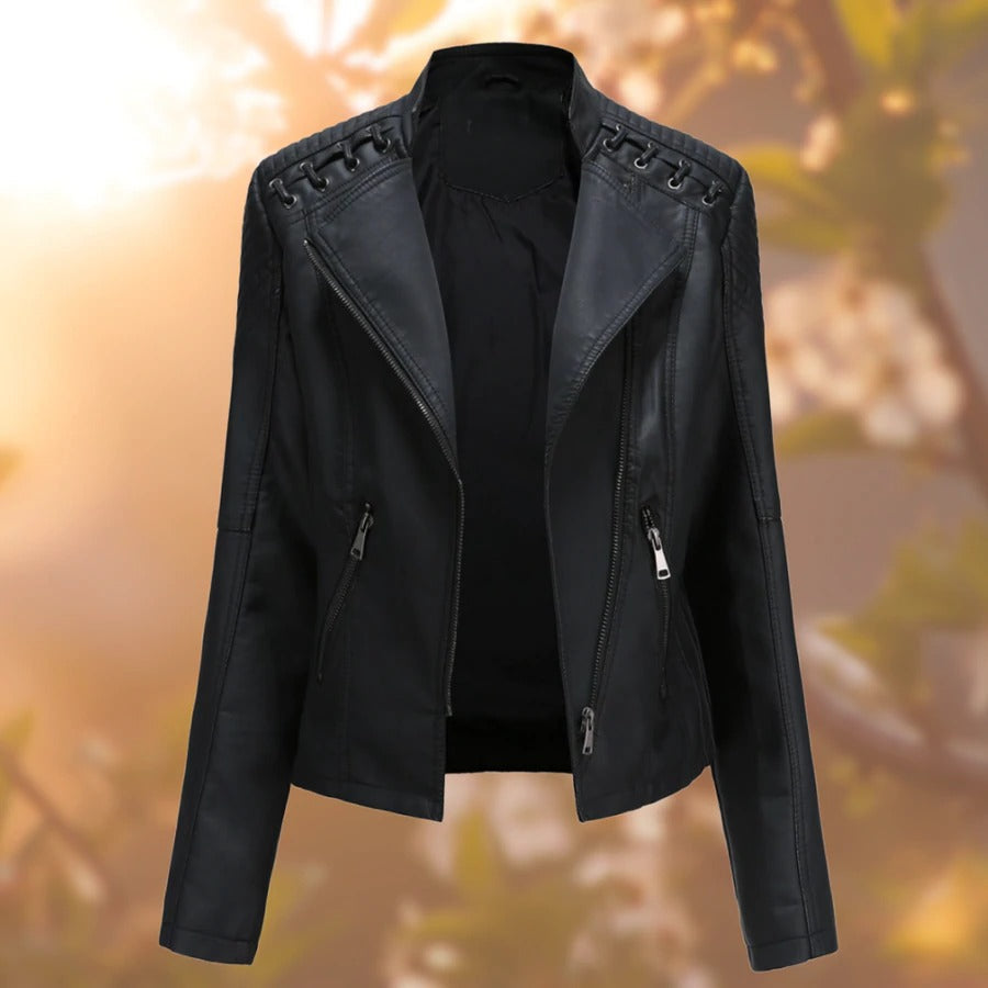 Giacca in pelle nera da donna con cerniere, design moderno e dettagli trapuntati sulle spalle, sfondo sfocato autunnale.