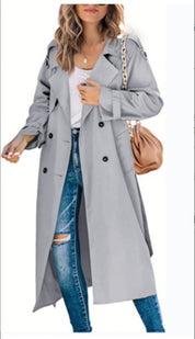 Cappotto trench donna grigio chiaro, doppio petto, abbinato a jeans strappati e borsa a tracolla beige. Moda autunnale elegante.