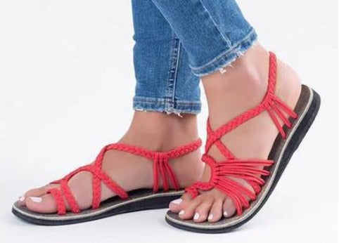 Sandali estivi rossi intrecciati da donna, suola piatta, indossati con jeans. Scarpe casual eleganti, ideali per la moda estiva.