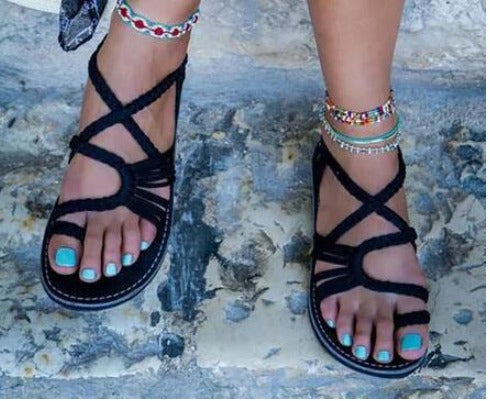 Sandali neri intrecciati su piedi con smalto turchese, cavigliere colorate. Moda estiva, calzature donna, accessori boho chic.