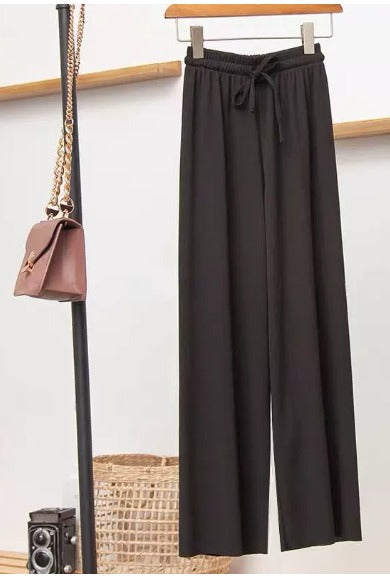 Pantaloni neri larghi appesi accanto a una borsa a tracolla marrone su sfondo bianco, moda casual elegante, abbigliamento donna.