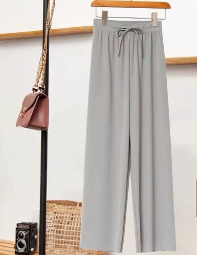 Pantaloni grigi eleganti appesi su appendiabiti, accanto a borsa a tracolla marrone e fotocamera vintage. Moda minimalista, abbigliamento casual chic.