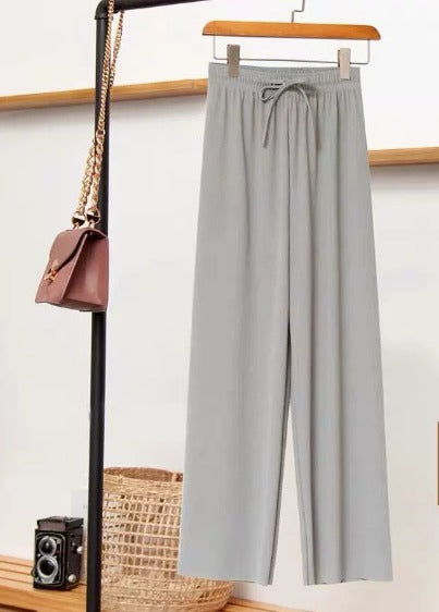 Pantaloni grigi eleganti appesi su appendiabiti, accanto a borsa a tracolla marrone e fotocamera vintage. Moda minimalista, abbigliamento casual chic.