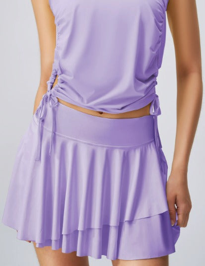 Abbigliamento sportivo donna: completo viola con top senza maniche e gonna a balze. Moda fitness, abbigliamento palestra, stile elegante.