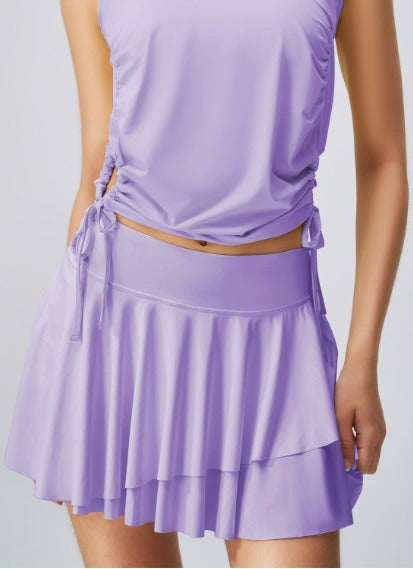 Abbigliamento sportivo donna: completo viola con top senza maniche e gonna a balze. Moda fitness, abbigliamento palestra, stile elegante.