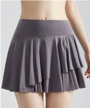 Gonna sportiva grigia a balze, indossata da una persona, vista posteriore. Abbigliamento fitness, moda donna, tessuto leggero e traspirante.