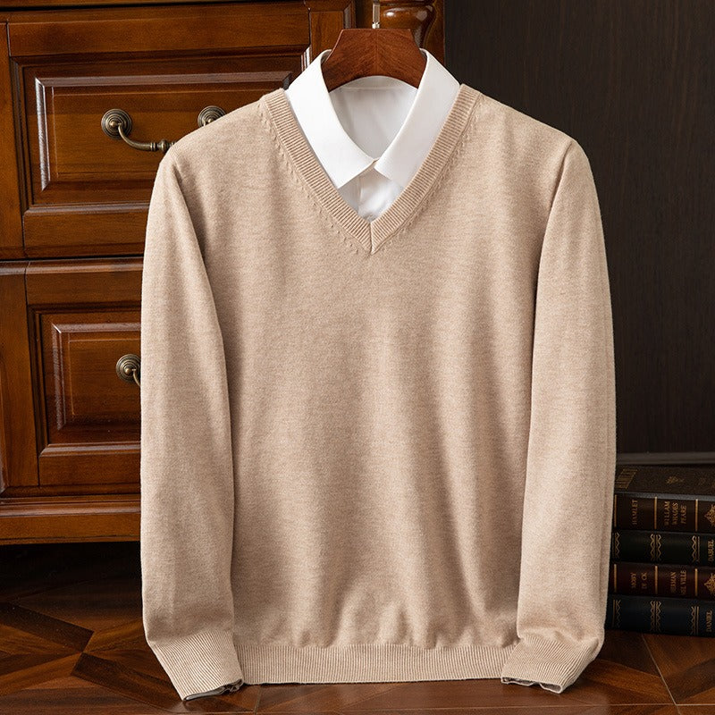 Maglione beige in cashmere con scollo a V su camicia bianca, appeso su gruccia di legno, davanti a cassetti in legno scuro. Elegante abbigliamento uomo.