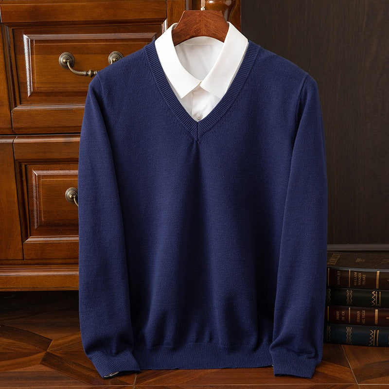 Maglione blu scuro con scollo a V su camicia bianca, appeso su gruccia di legno. Elegante abbigliamento maschile, moda autunnale, stile classico.