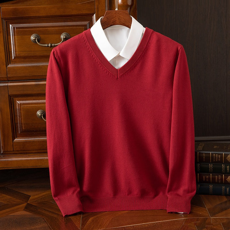 Maglione rosso con scollo a V su camicia bianca, appeso su gruccia di legno. Sfondo con cassetti in legno e libri. Moda elegante e classica.