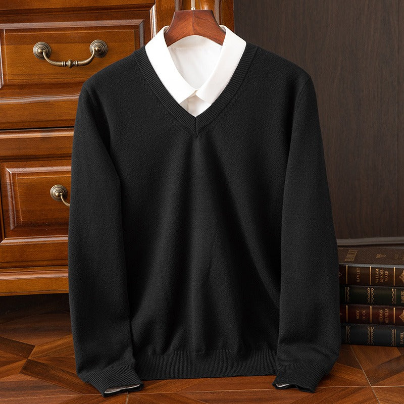Maglione nero elegante con scollo a V su camicia bianca, appeso su gruccia di legno, davanti a cassettiera in legno. Moda uomo, abbigliamento classico.