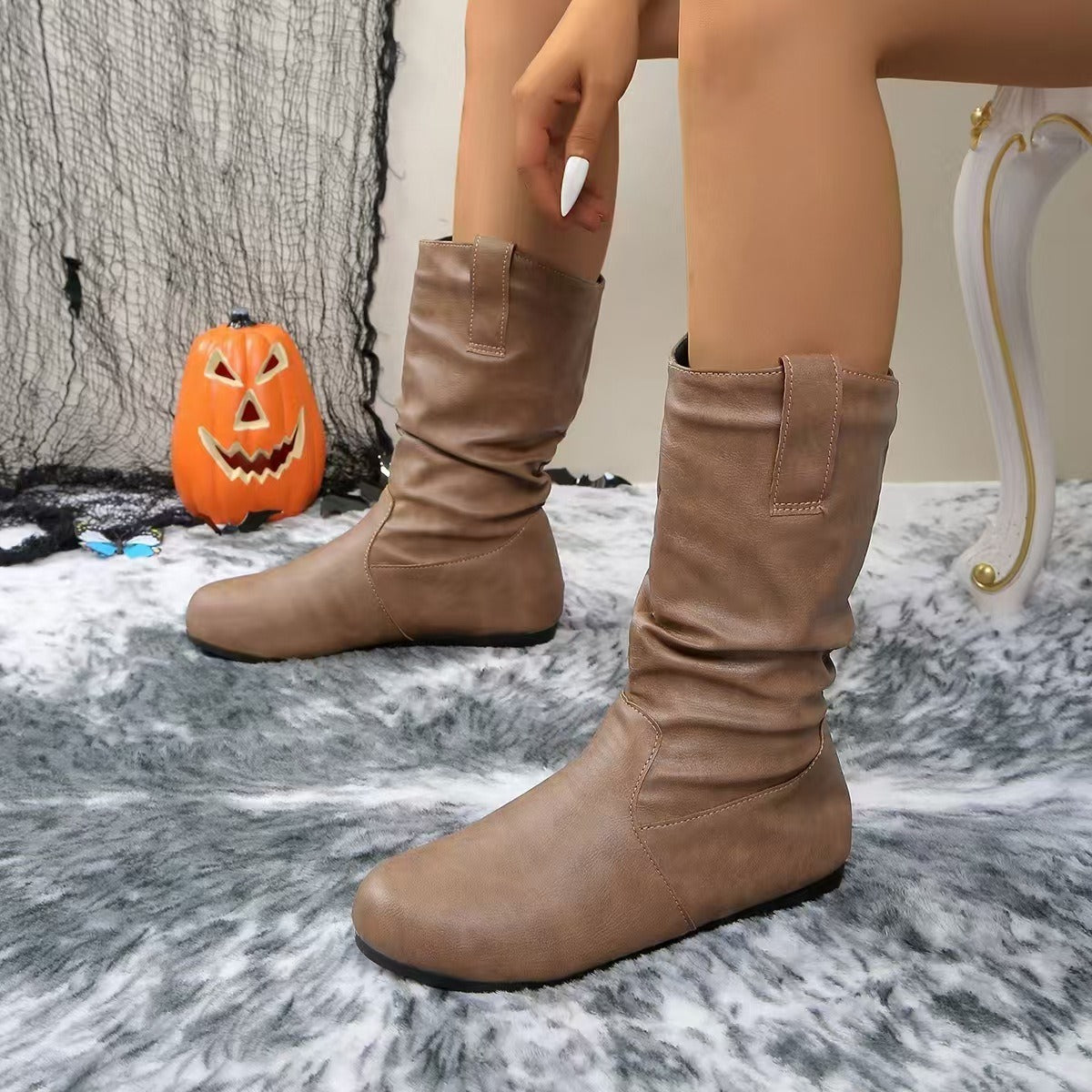 Stivali marroni in pelle su tappeto grigio, decorazione di Halloween con zucca intagliata sullo sfondo. Scarpe autunnali eleganti e comode.