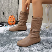Stivali marroni in pelle su tappeto grigio, decorazione di Halloween con zucca intagliata sullo sfondo. Scarpe autunnali eleganti e comode.