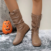 Stivali marroni in pelle su tappeto grigio, decorazione di Halloween con zucca intagliata sullo sfondo. Scarpe autunnali eleganti e comode.