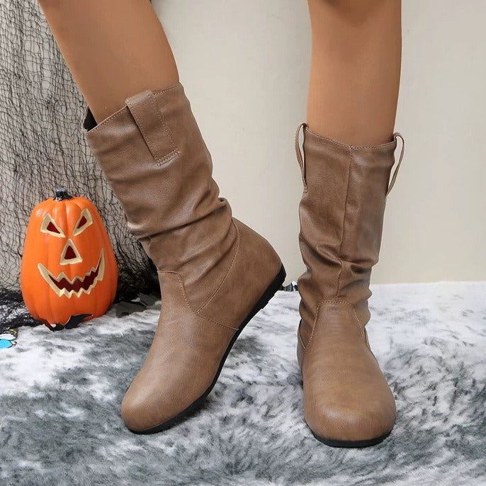 Stivali marroni in pelle su tappeto grigio, decorazione di Halloween con zucca intagliata sullo sfondo. Scarpe autunnali eleganti e comode.