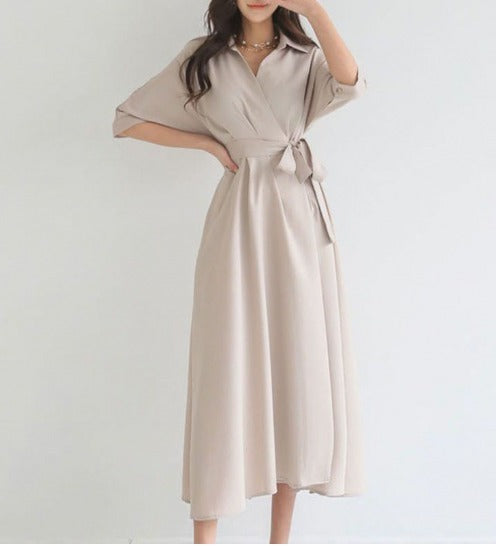 Abito lungo beige elegante, con cintura in vita e maniche a tre quarti, indossato da una donna. Perfetto per moda femminile e occasioni formali.