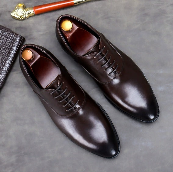 Scarpe eleganti da uomo in pelle marrone scuro, con lacci, su sfondo grigio. Accessori di lusso visibili, ideale per abbigliamento formale.