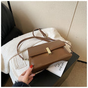 Borsa a tracolla marrone su sedia bianca, design elegante con chiusura dorata. Accessorio moda donna, stile casual chic.