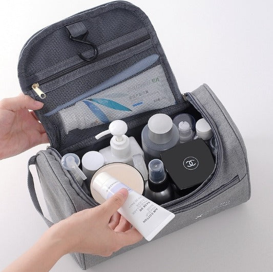 Borsa da toilette grigia aperta con prodotti cosmetici e per la cura della pelle, tra cui flaconi e creme, su sfondo bianco.