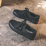 Scarpe da ginnastica nere su pavimento grigio, design casual con lacci. Calzature moda uomo, stile urbano, comfort quotidiano.