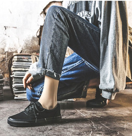 Jeans strappati e scarpe da ginnastica nere su sfondo urbano. Moda casual, stile streetwear, abbigliamento giovanile.
