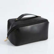 Borsa da toilette nera in pelle sintetica con cerniera e manico superiore, ideale per viaggi e organizzazione cosmetici. Design elegante e pratico.