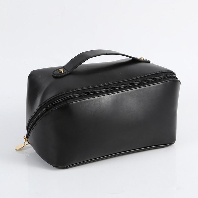 Borsa da toilette nera in pelle sintetica con cerniera e manico superiore, ideale per viaggi e organizzazione cosmetici. Design elegante e pratico.