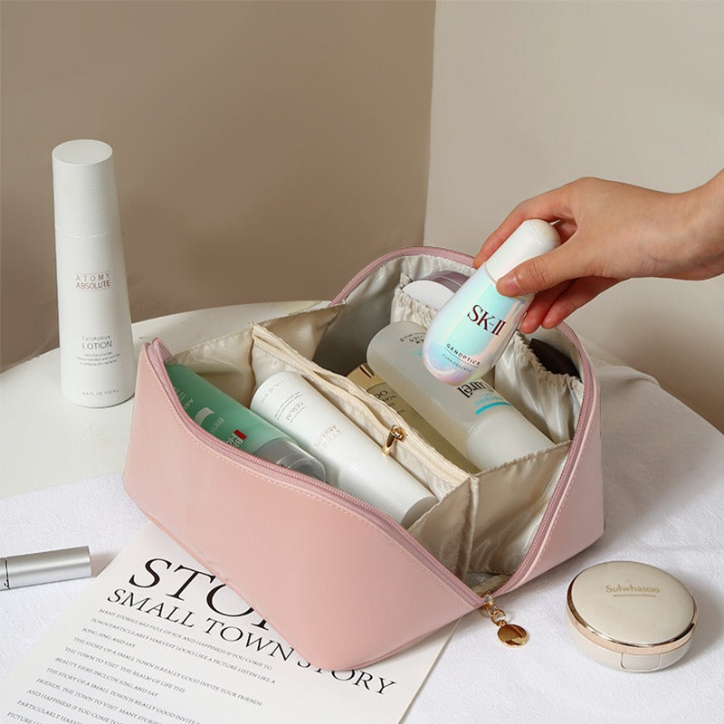 Beauty case rosa con prodotti skincare: flaconi di lozioni, creme e sieri. Mano che prende una bottiglia SK-II. Tavolo bianco, ambiente elegante.