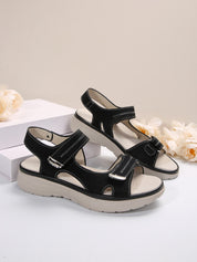 Sandali neri da donna con suola spessa beige, design sportivo, chiusura a strappo, su sfondo neutro con fiori bianchi.